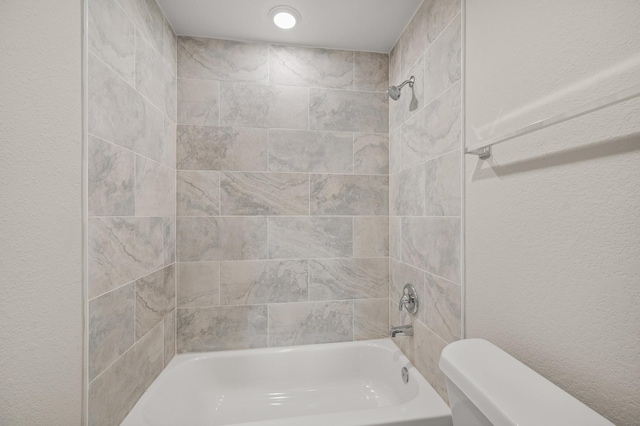 bathroom featuring washtub / shower combination, a textured wall, and toilet