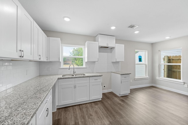 kitchen featuring dark wood-style flooring, white cabinets, a sink, light stone countertops, and baseboards