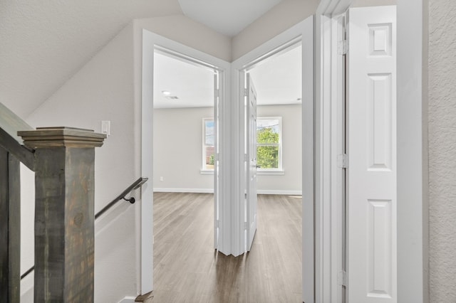 hallway with a textured wall, wood finished floors, an upstairs landing, and baseboards