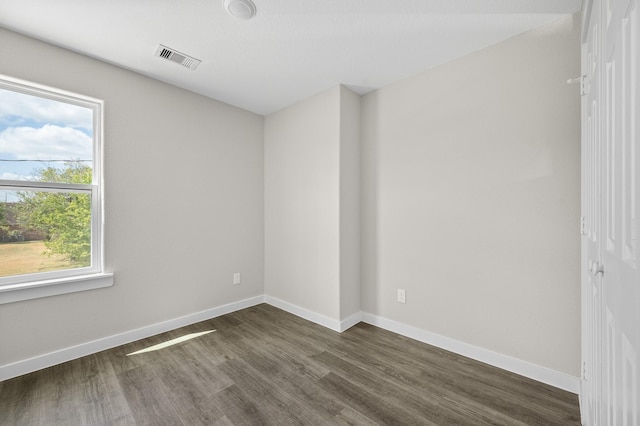 empty room featuring dark wood-style floors, visible vents, and baseboards