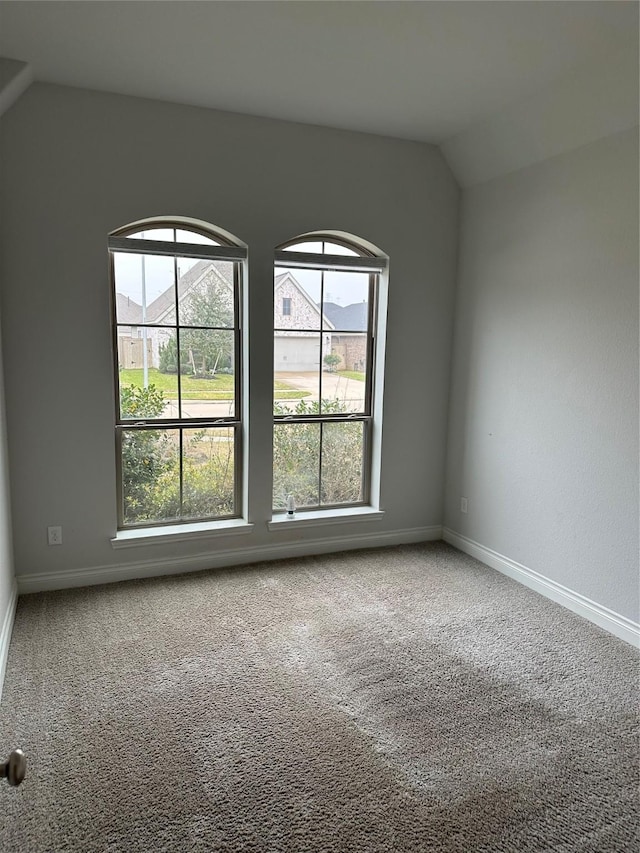 carpeted empty room with baseboards and vaulted ceiling