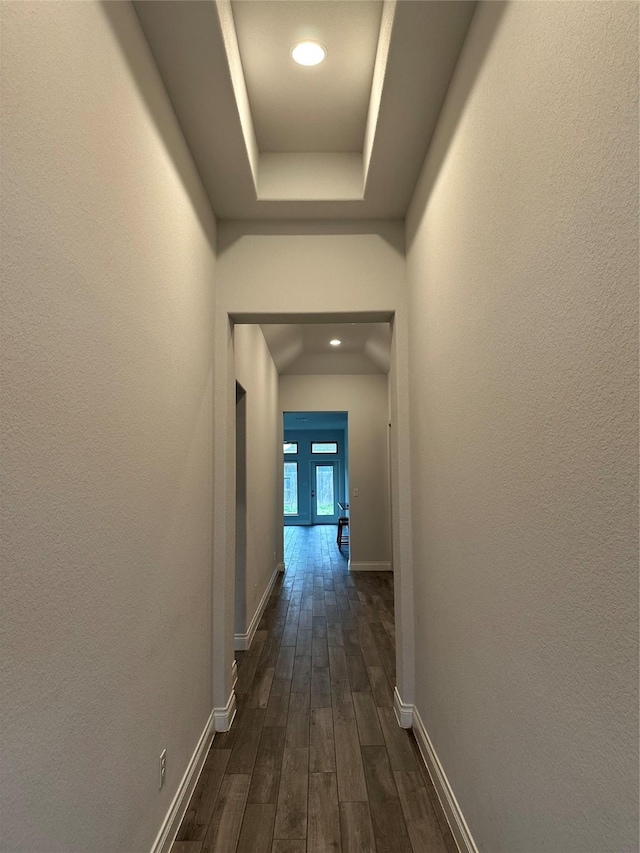 hall with a textured wall, a tray ceiling, dark wood finished floors, and baseboards