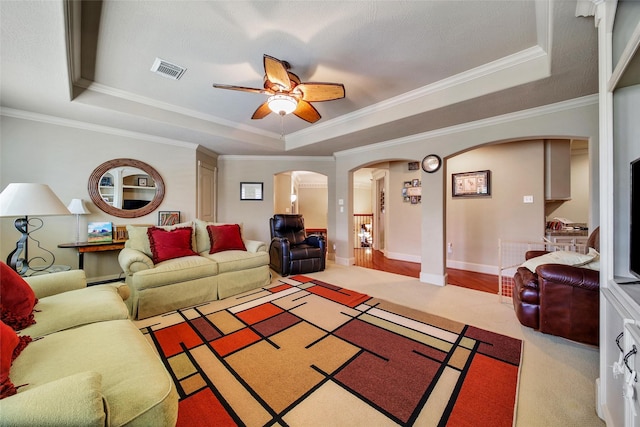 carpeted living room featuring visible vents, arched walkways, a raised ceiling, a ceiling fan, and ornamental molding