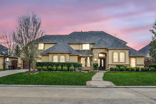 french provincial home featuring driveway, stone siding, a front yard, and stucco siding