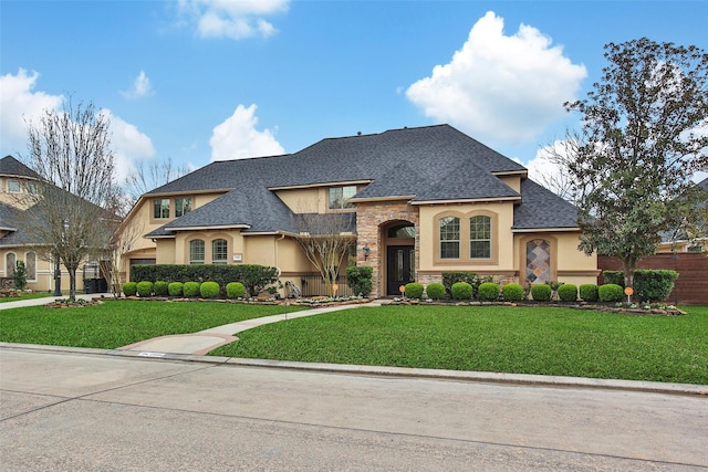 french country home with stone siding, a shingled roof, a front yard, and stucco siding