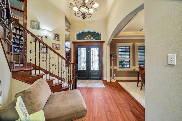 foyer entrance with baseboards, arched walkways, wood finished floors, stairs, and a notable chandelier