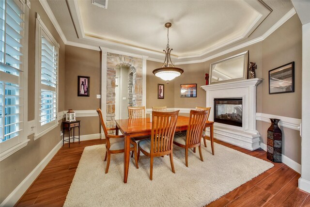 dining room with a raised ceiling, visible vents, a multi sided fireplace, wood finished floors, and baseboards