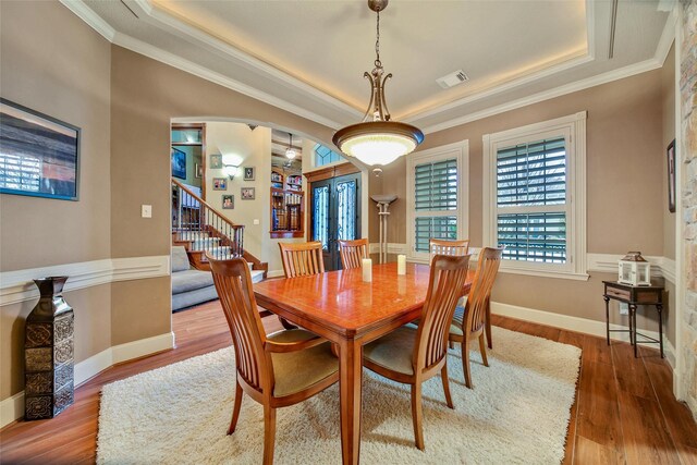 dining room with arched walkways, crown molding, a raised ceiling, visible vents, and wood finished floors