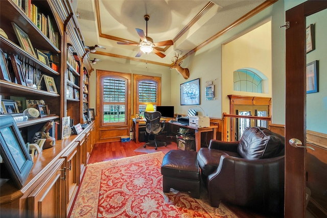 office area with a wainscoted wall, wood finished floors, a ceiling fan, a raised ceiling, and crown molding