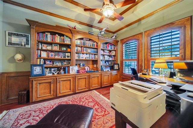 office with a wainscoted wall, a raised ceiling, ornamental molding, a ceiling fan, and light wood-type flooring