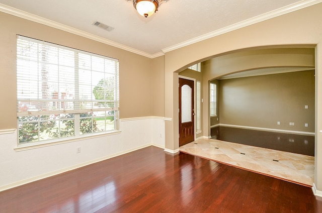 entrance foyer featuring arched walkways, wood finished floors, visible vents, baseboards, and ornamental molding