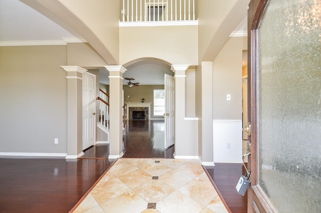 entryway featuring wood finished floors, a high end fireplace, a ceiling fan, ornamental molding, and decorative columns