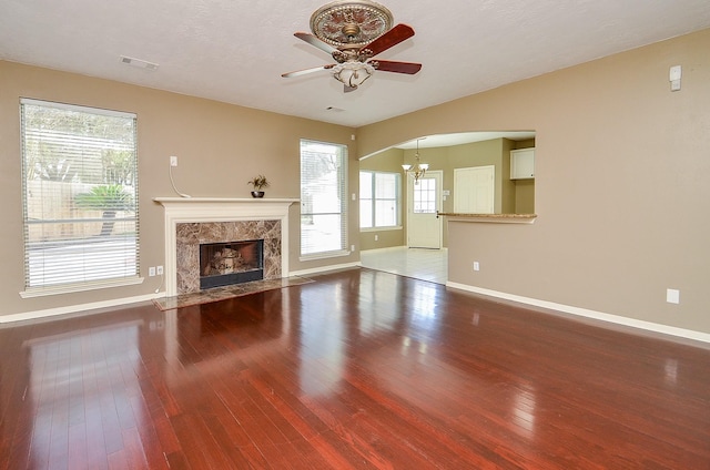 unfurnished living room with hardwood / wood-style flooring, visible vents, a high end fireplace, baseboards, and ceiling fan with notable chandelier