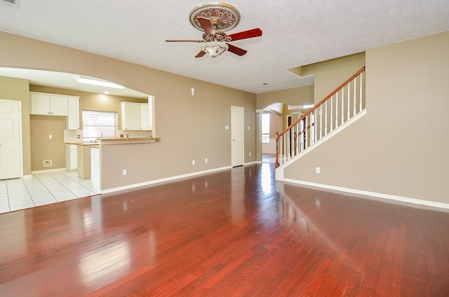 unfurnished living room with light wood-type flooring, arched walkways, stairway, and baseboards