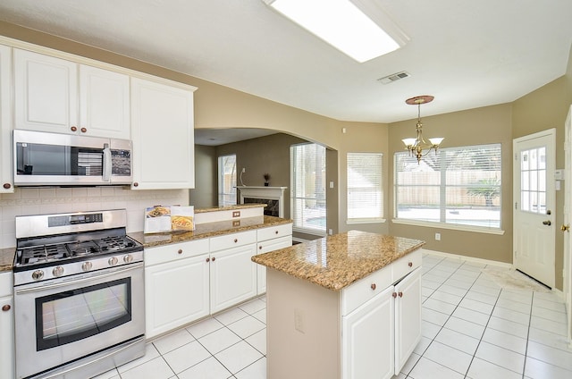 kitchen with light tile patterned floors, stainless steel gas range oven, visible vents, tasteful backsplash, and decorative light fixtures