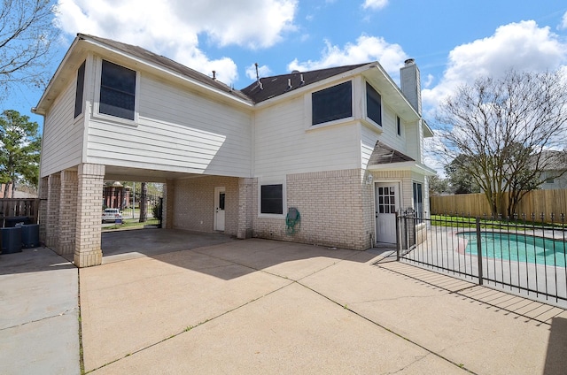 back of property with a carport, brick siding, a chimney, and fence