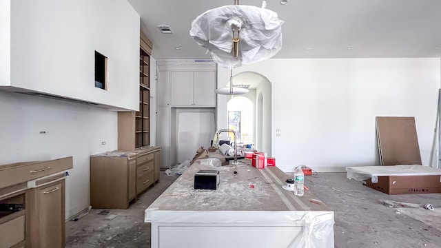 kitchen featuring arched walkways, light countertops, visible vents, white cabinetry, and a sink