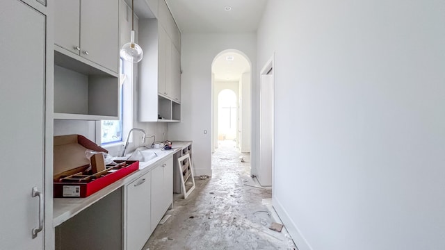 kitchen featuring arched walkways, a sink, baseboards, white cabinets, and light countertops