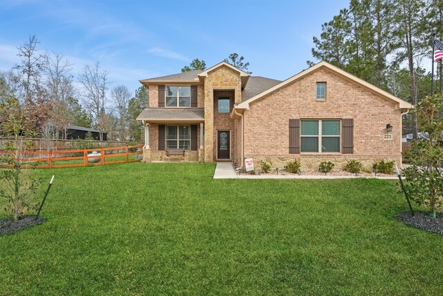 view of front facade with brick siding, fence, stone siding, roof with shingles, and a front lawn