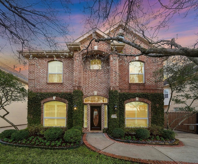 view of front of home featuring brick siding, driveway, and fence