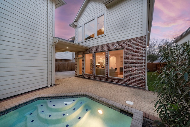 pool at dusk with a patio area and fence