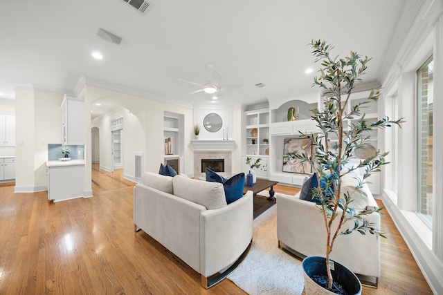 living room featuring visible vents, light wood finished floors, a fireplace, arched walkways, and crown molding