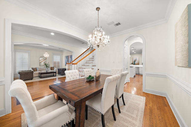 dining room with light wood-type flooring, visible vents, ornamental molding, arched walkways, and stairs