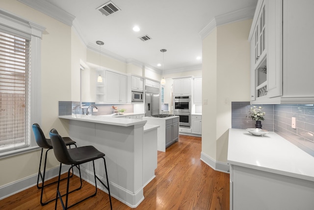 kitchen featuring built in appliances, a peninsula, crown molding, and visible vents