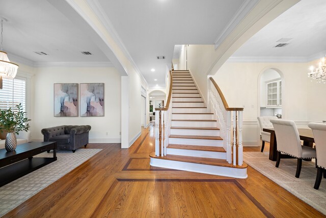 stairs featuring visible vents, a chandelier, ornamental molding, wood finished floors, and arched walkways