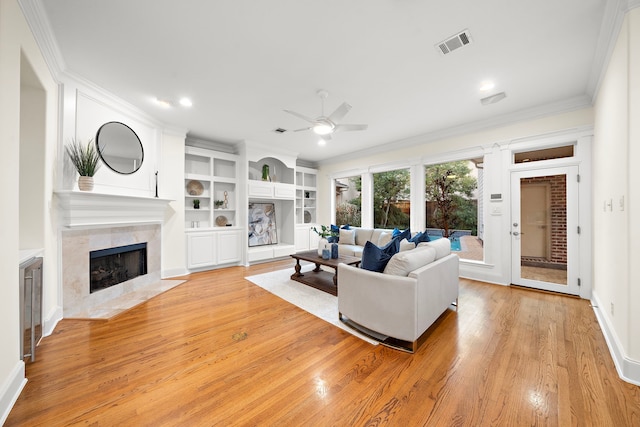 living room featuring a ceiling fan, visible vents, light wood finished floors, ornamental molding, and a tiled fireplace