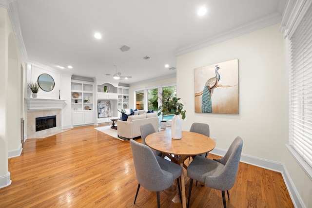 dining space with ornamental molding, light wood-style flooring, recessed lighting, a premium fireplace, and baseboards