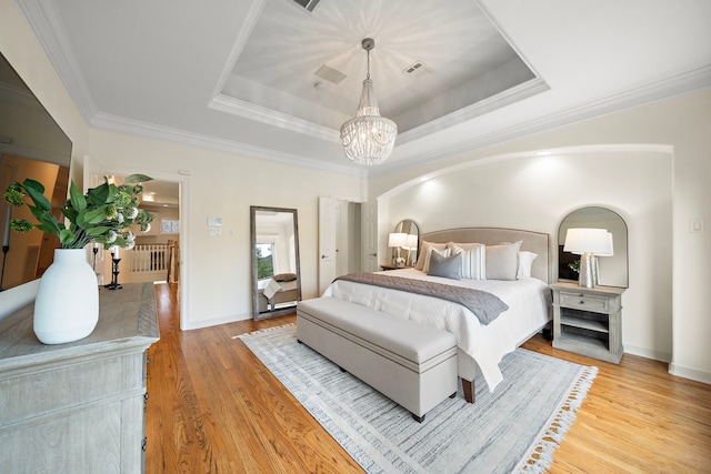 bedroom featuring visible vents, light wood-style flooring, a tray ceiling, and ornamental molding