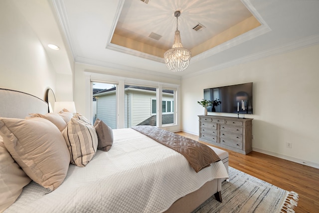 bedroom with visible vents, a tray ceiling, wood finished floors, crown molding, and baseboards