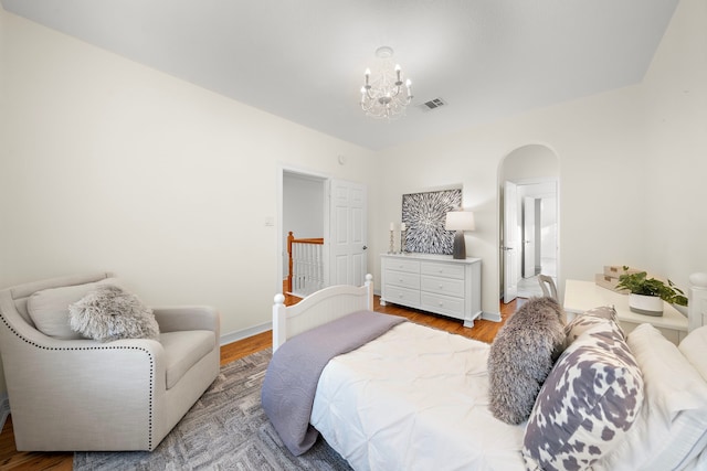 bedroom with wood finished floors, baseboards, visible vents, arched walkways, and a chandelier