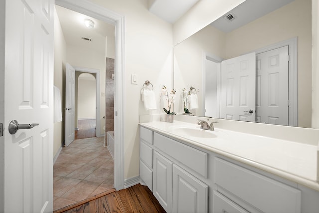 bathroom featuring visible vents, tiled shower, baseboards, and vanity