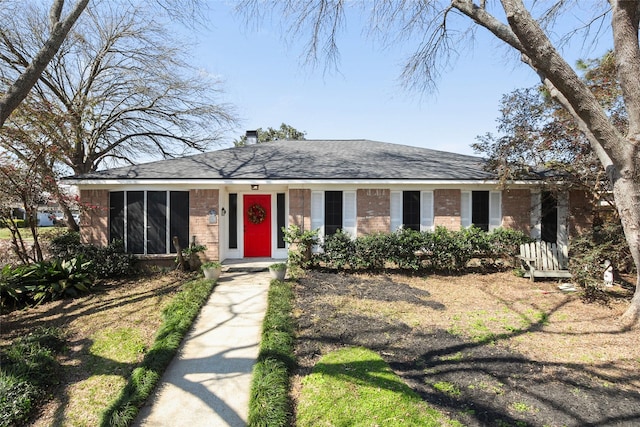 view of front of home with a sunroom, brick siding, and roof with shingles