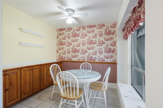 dining room featuring light tile patterned floors, a textured ceiling, wainscoting, and wallpapered walls