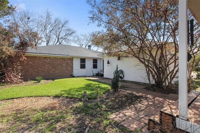 view of front of property featuring brick siding, a front lawn, and roof with shingles