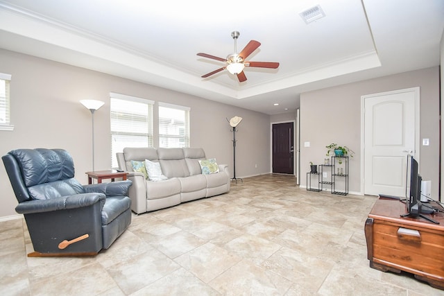 living area with a ceiling fan, baseboards, visible vents, a tray ceiling, and ornamental molding