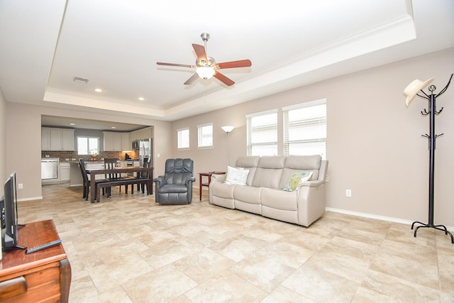 living area with a tray ceiling, a ceiling fan, baseboards, and ornamental molding