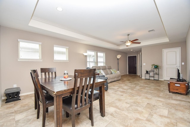 dining room with a tray ceiling, baseboards, visible vents, and ceiling fan