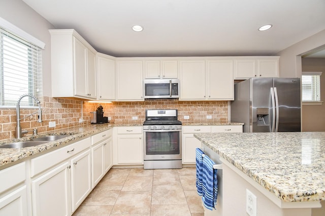 kitchen featuring light tile patterned floors, a sink, stainless steel appliances, white cabinets, and backsplash