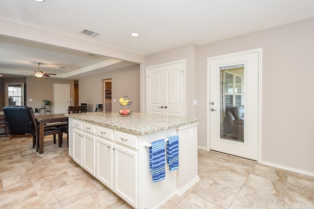 kitchen with a center island, white cabinetry, baseboards, and light stone countertops