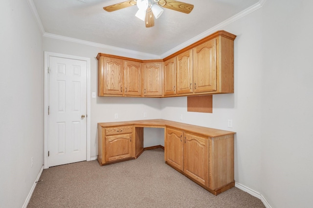 unfurnished office featuring ceiling fan, light carpet, baseboards, built in desk, and crown molding