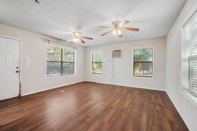 unfurnished room with dark wood-style flooring, a wall unit AC, a ceiling fan, and baseboards