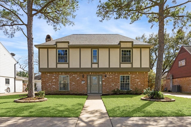 view of front facade featuring a front yard, brick siding, a chimney, and stucco siding