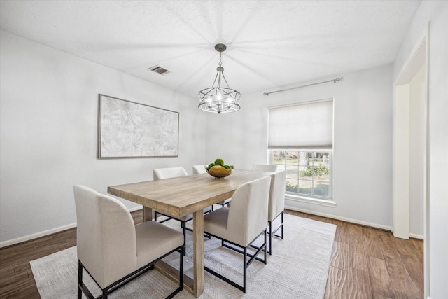 dining space featuring an inviting chandelier, wood finished floors, visible vents, and baseboards