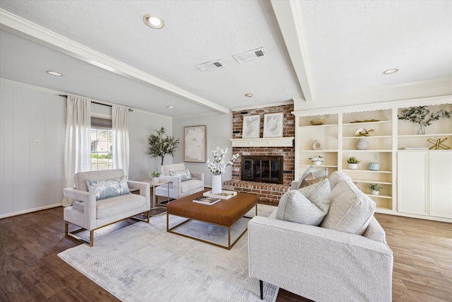 living area with beamed ceiling, a brick fireplace, wood finished floors, and visible vents