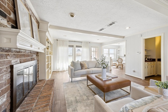 living room featuring a brick fireplace, a textured ceiling, visible vents, and wood finished floors