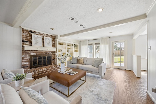 living room with a brick fireplace, a textured ceiling, visible vents, and beamed ceiling